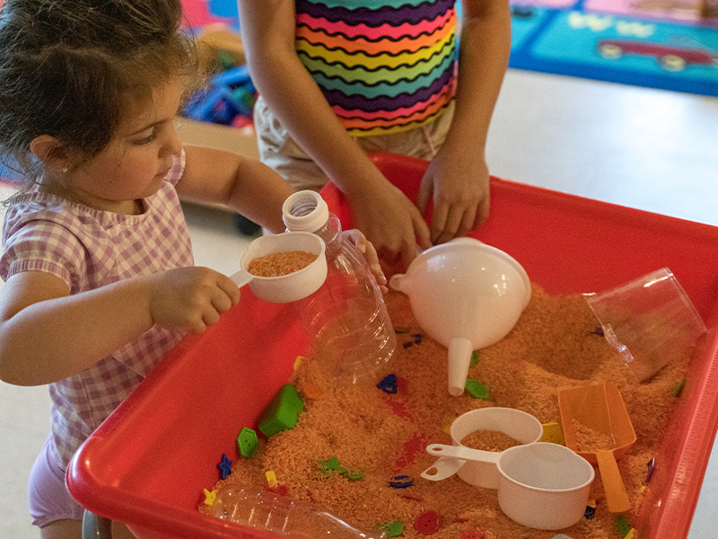 Child playing with sand, measuring cups, funnels, and more.