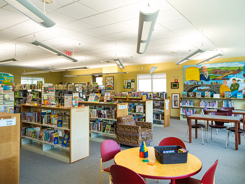 Children's department with many bookcases full of books for children as well as table for crafts and games.