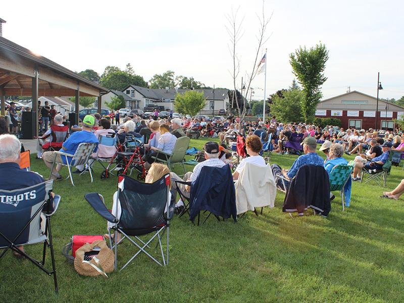 Concert series, wide shot of a crowd of listeners as well as performers on stage.